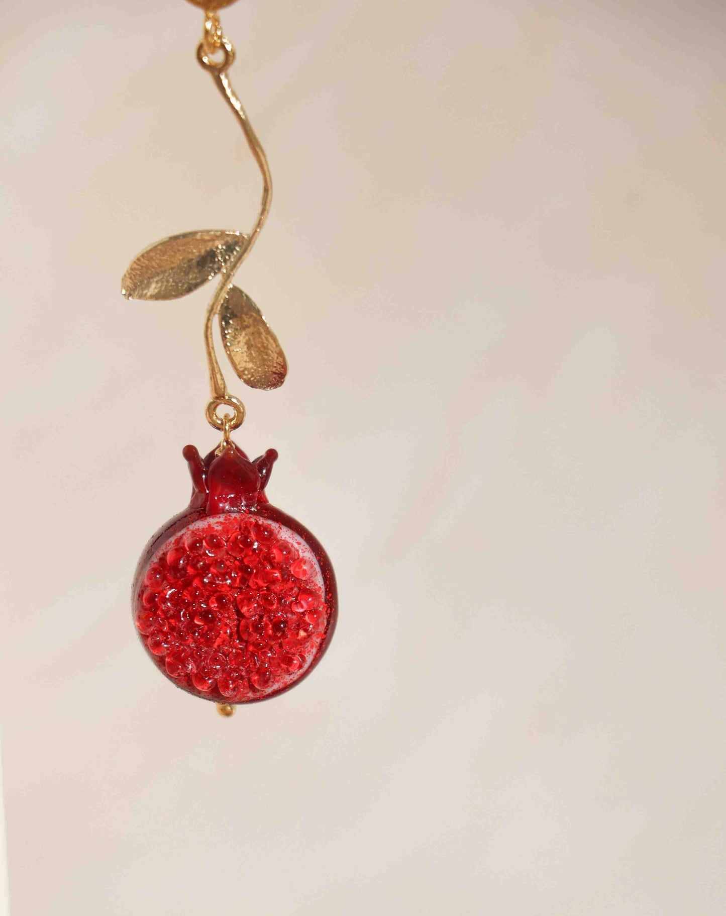 A red and gold fruit earrring on a pink background