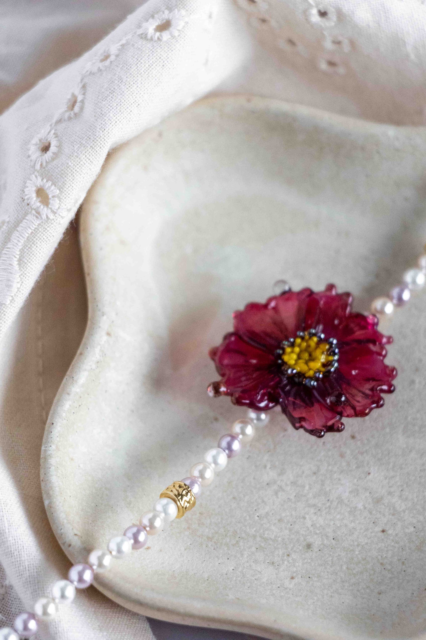 Mother of pearl necklace with a red flower pendant on a textured surface