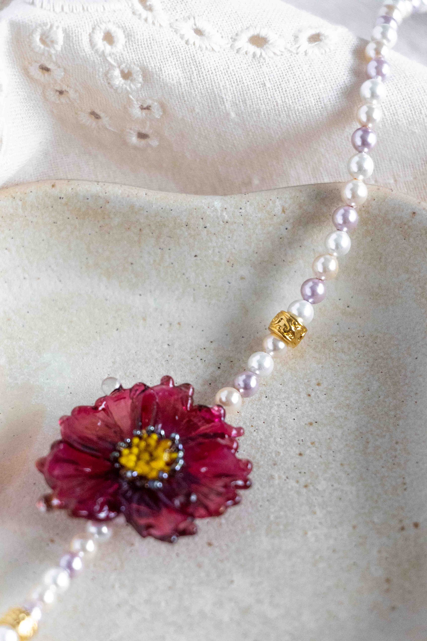 Necklace with a pink flower pendant on a textured surface. Close up to the details.