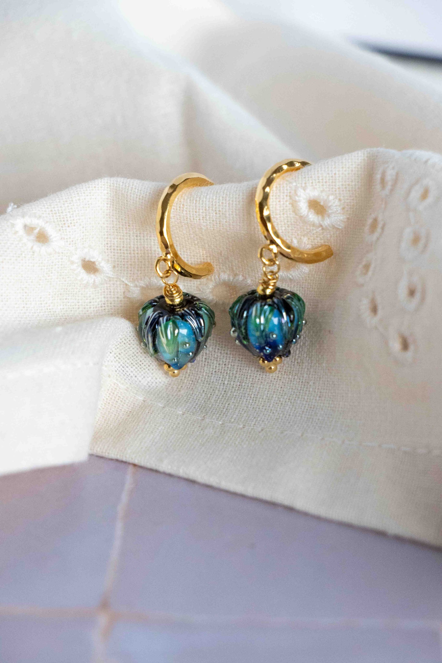Gold earrings with blue-green beads on a white fabric background