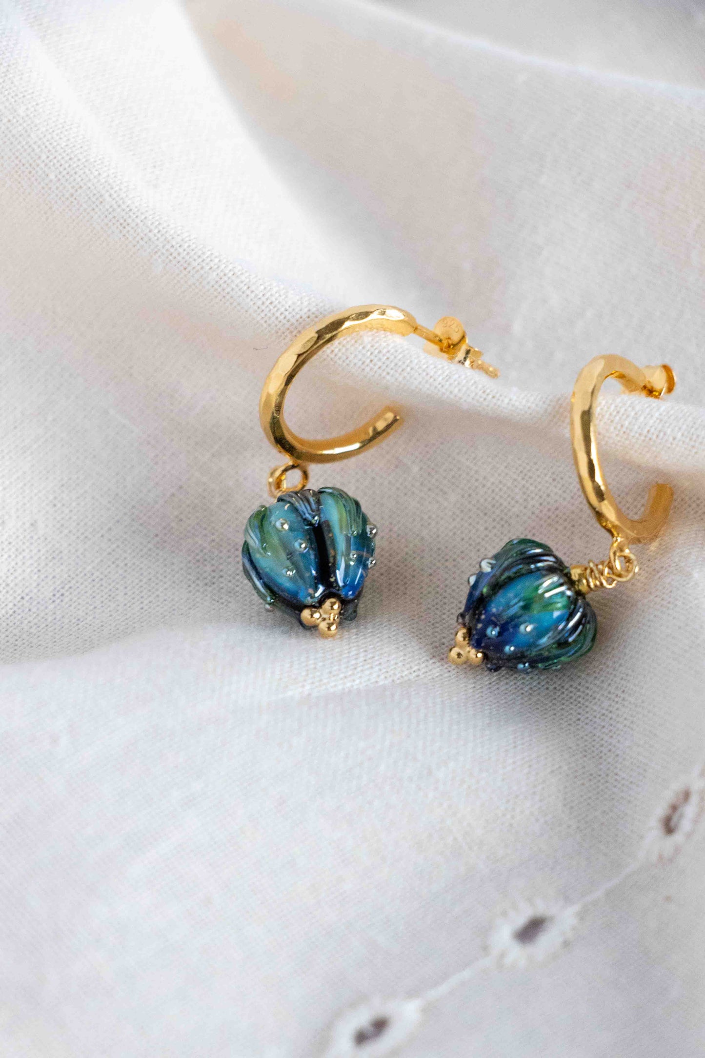 Gold hoop earrings with blue flowers on a white fabric background