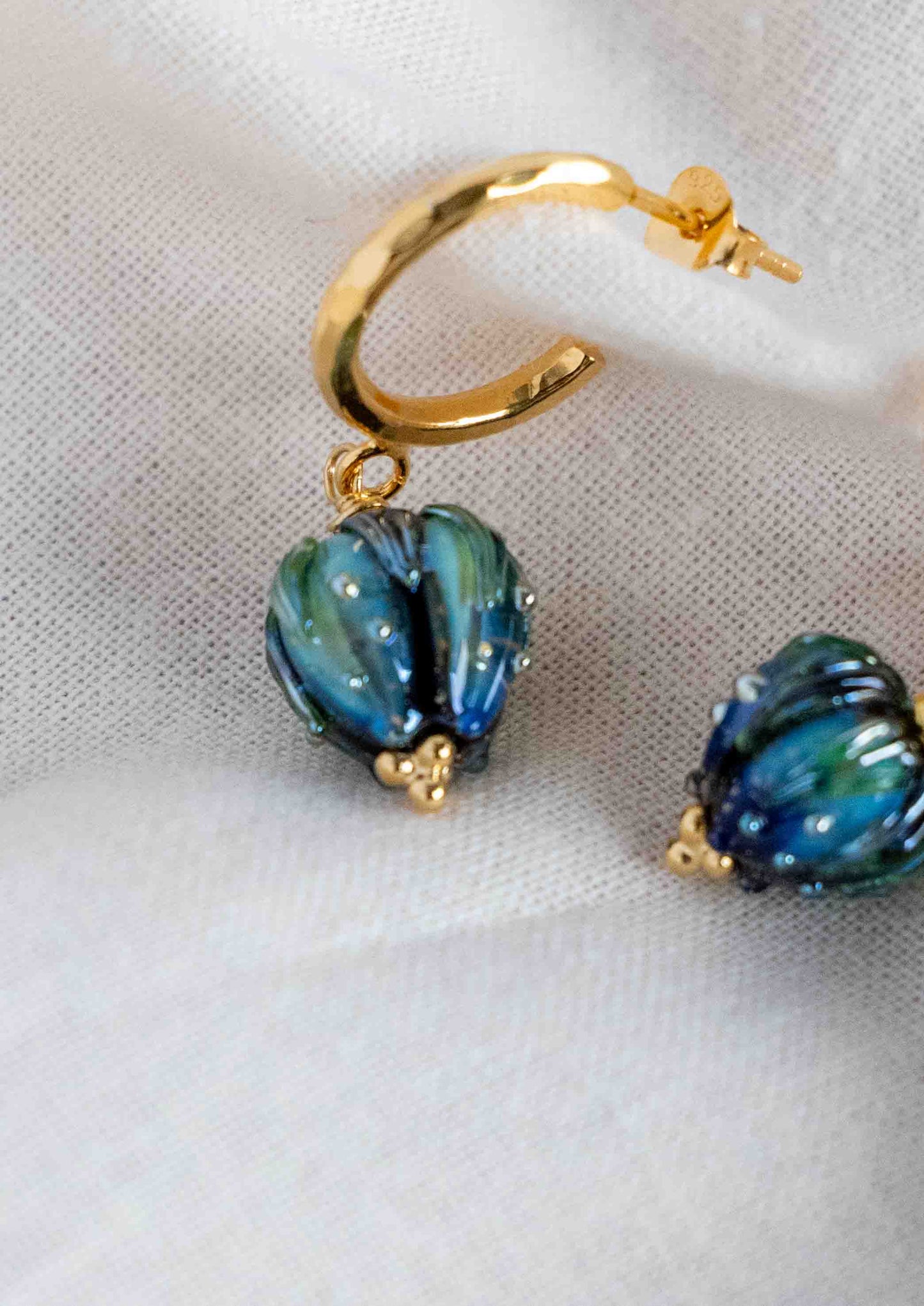 Gold hoop earrings with blue and green flowers on a white fabric background