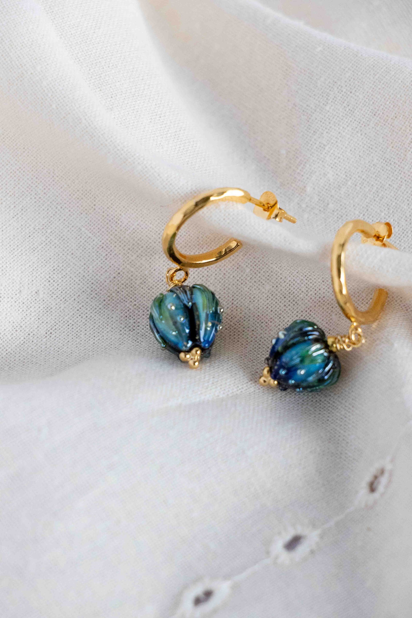 Gold hoop earrings with blue mystical flowers on a white fabric background
