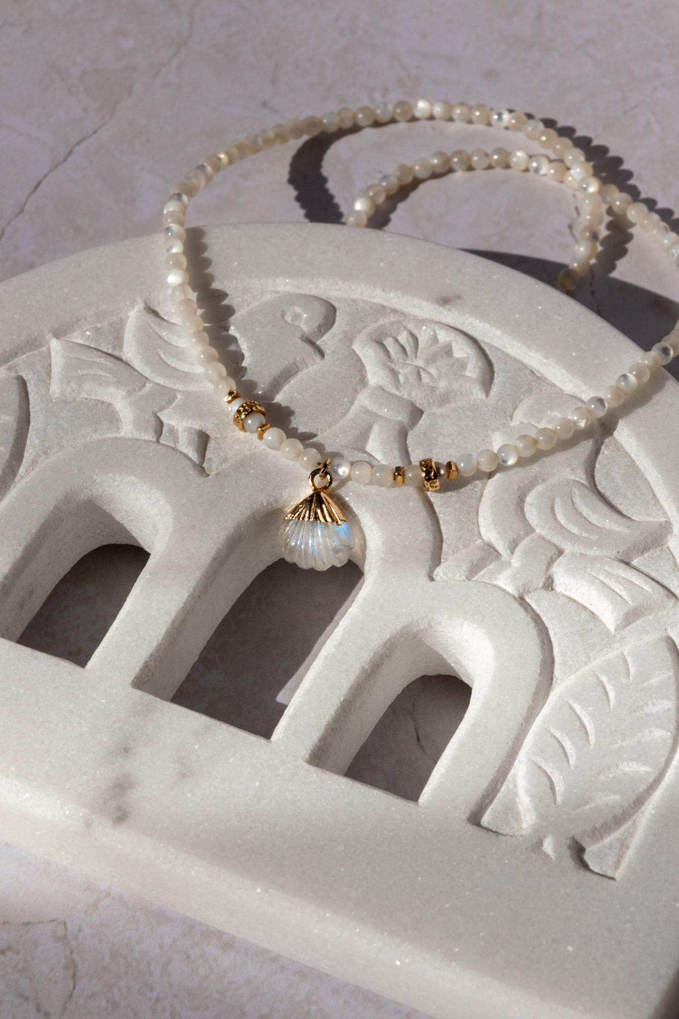 The cycladic Shell Neckace placed on a piece of curved marble from Tinos Island in Greece