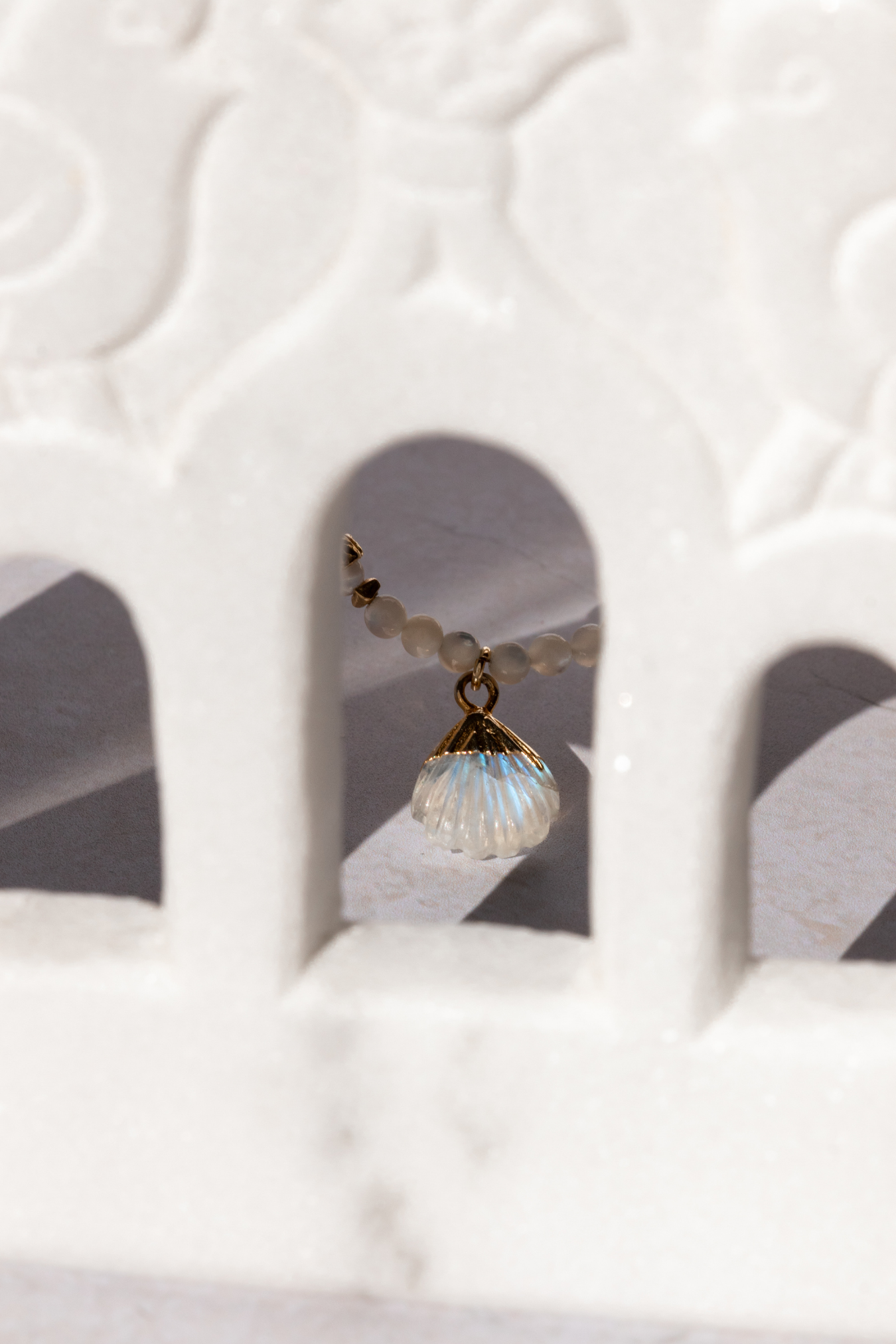 The cycladic Shell Neckace seen through a small window. The flashy moonrock is reflecting the light in blue hues.