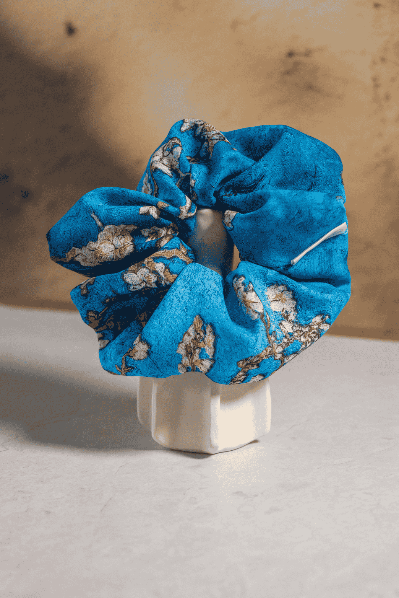Blue floral scrunchie on a white stand against a wooden background
