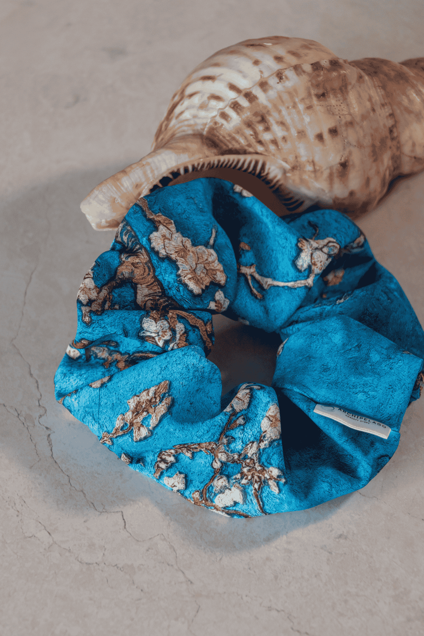 Blue scrunchie with floral pattern inside a shell on a textured surface