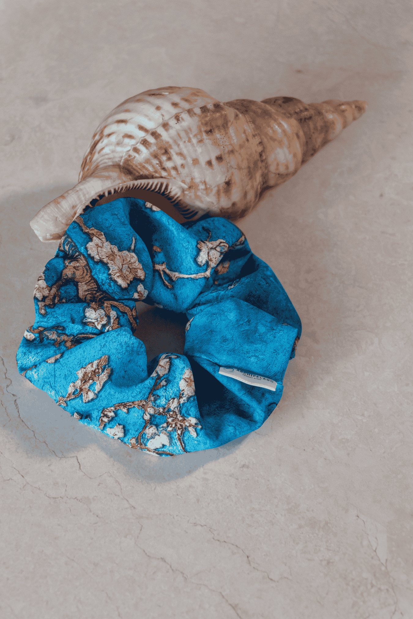 Blue scrunchie with floral pattern on a shell against a beige background