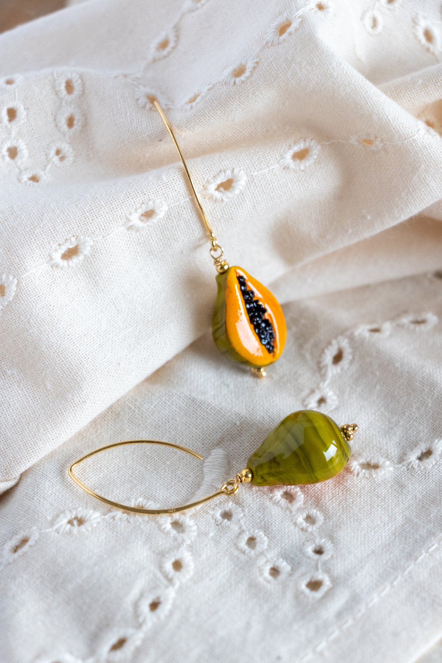 Two teardrop-shaped papaya fruit earrings on a white fabric background