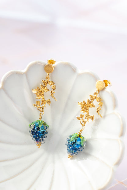 Gold earrings with blue grape beads on a white shell