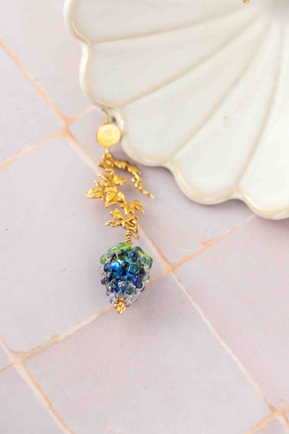 Gold earring with blue grapes on a decorative white surface