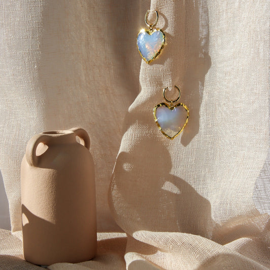 A pair of two opalite heart earrings in a blue hue. 