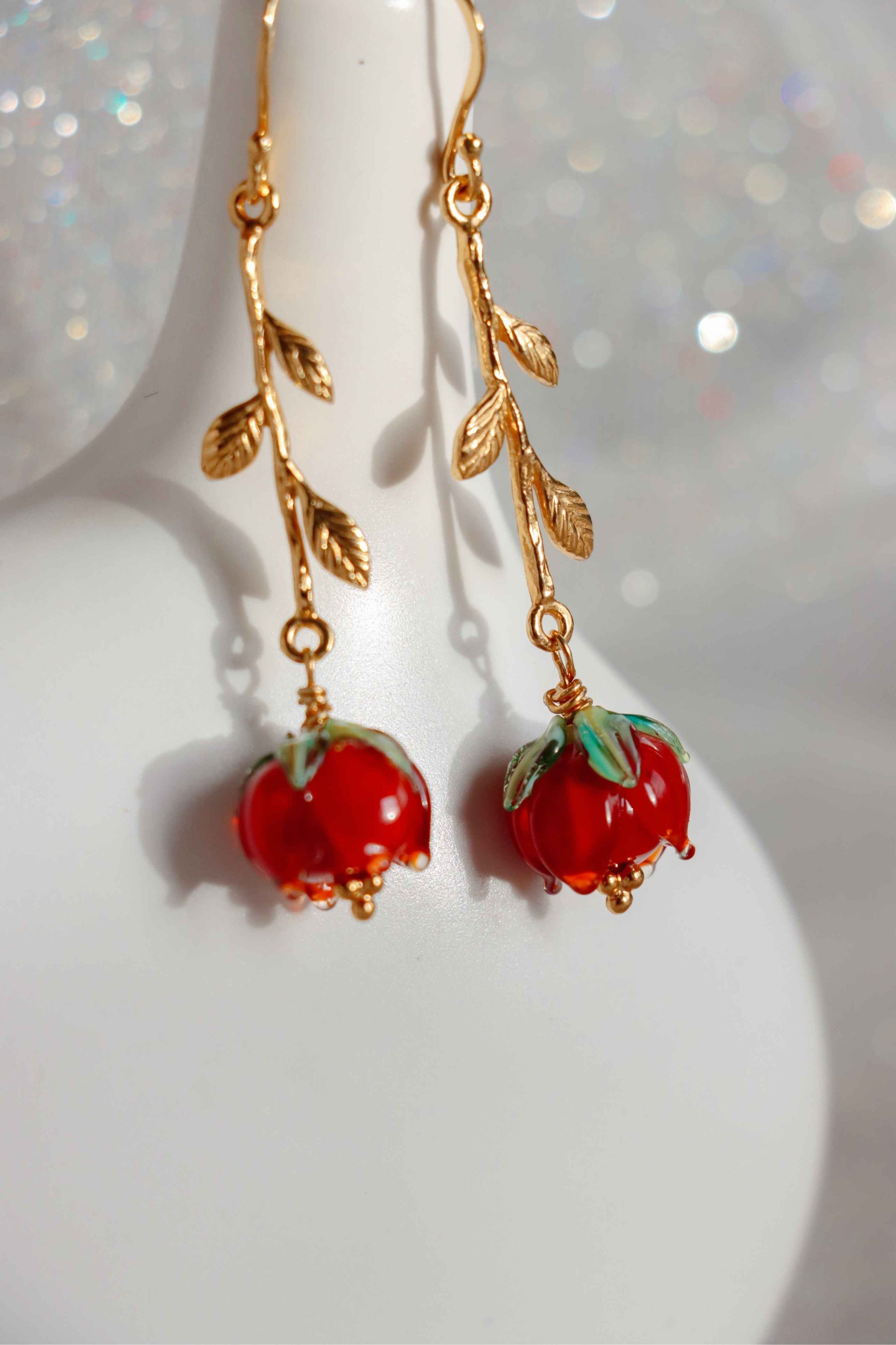 A pair of earrings shaped like roses. They are about 8cm long made of silver and glass red roses. A close up to the gold details of the leaves of the roses.