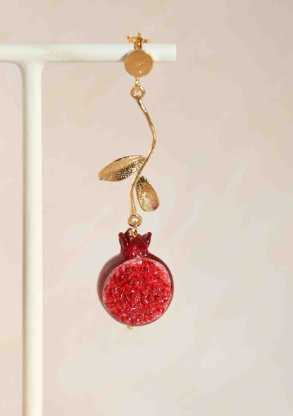 A red fruit earring with gold on a light pink backround