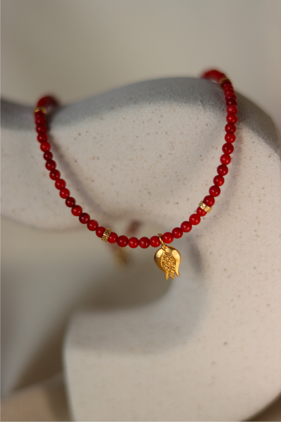 a red necklalce with a golden pomegranade charm