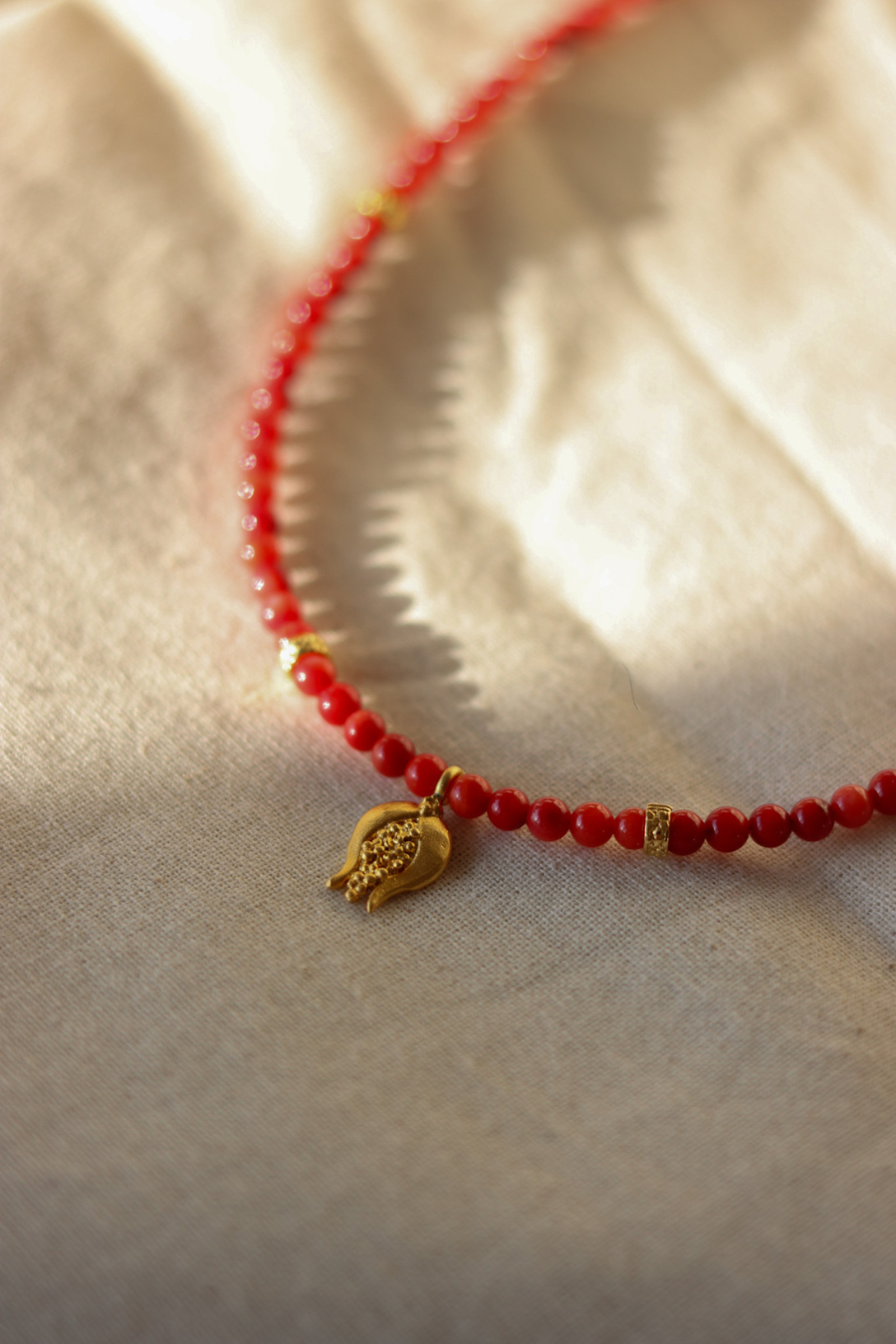 a red necklalce with a golden pomegranade charm