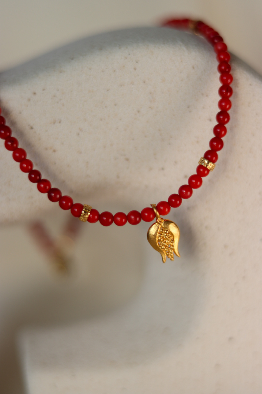 a red necklalce with a golden pomegranade charm