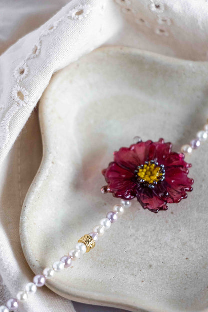 Mother of pearl necklace with a red flower pendant on a textured surface