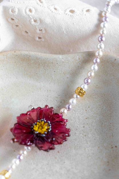 Necklace with a pink flower pendant on a textured surface. Close up to the details.