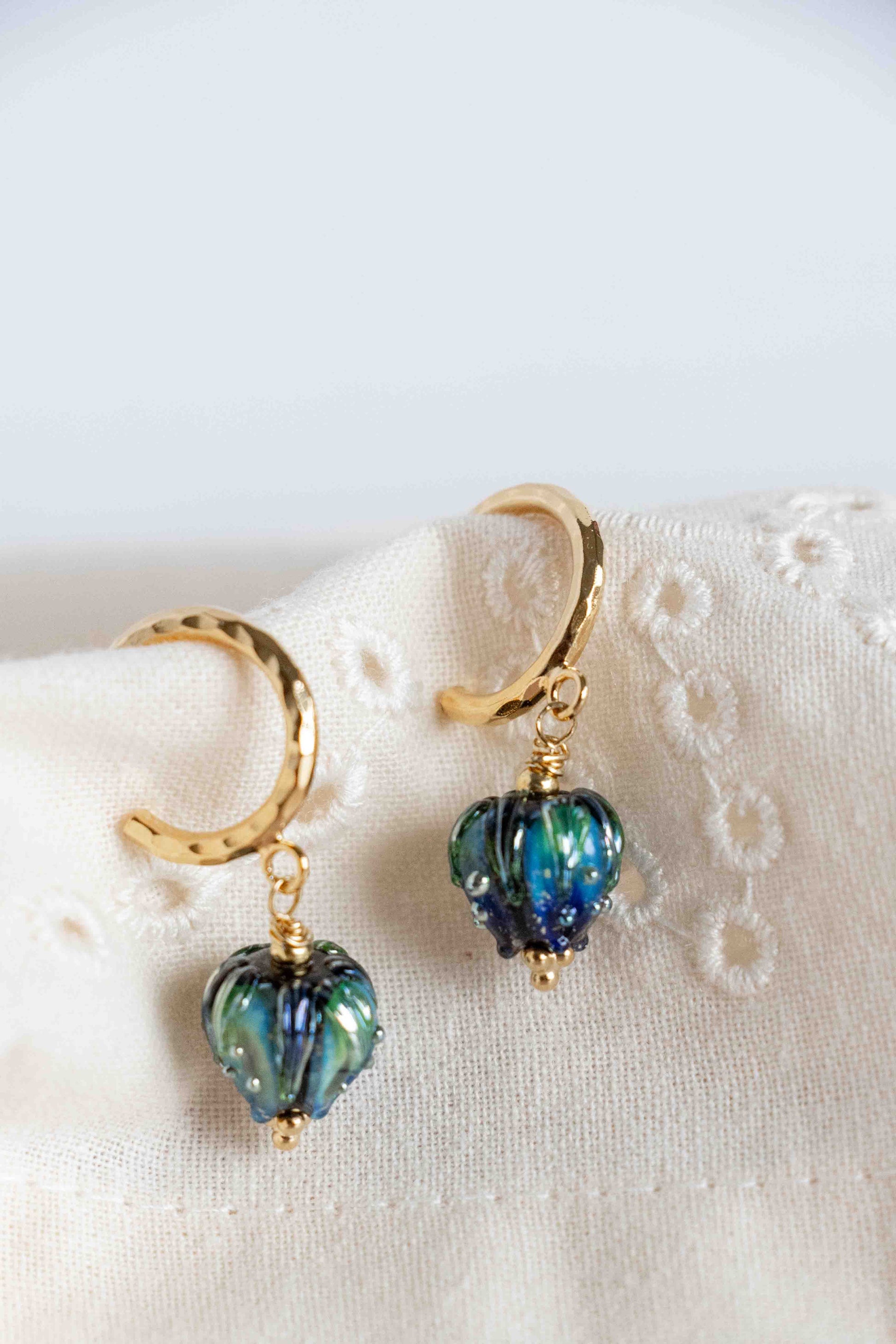 Pair of gold earrings with blue heart-shaped beads on a white fabric background