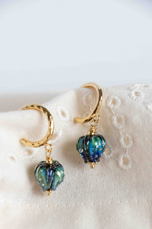 Pair of gold earrings with blue heart-shaped beads on a white fabric background