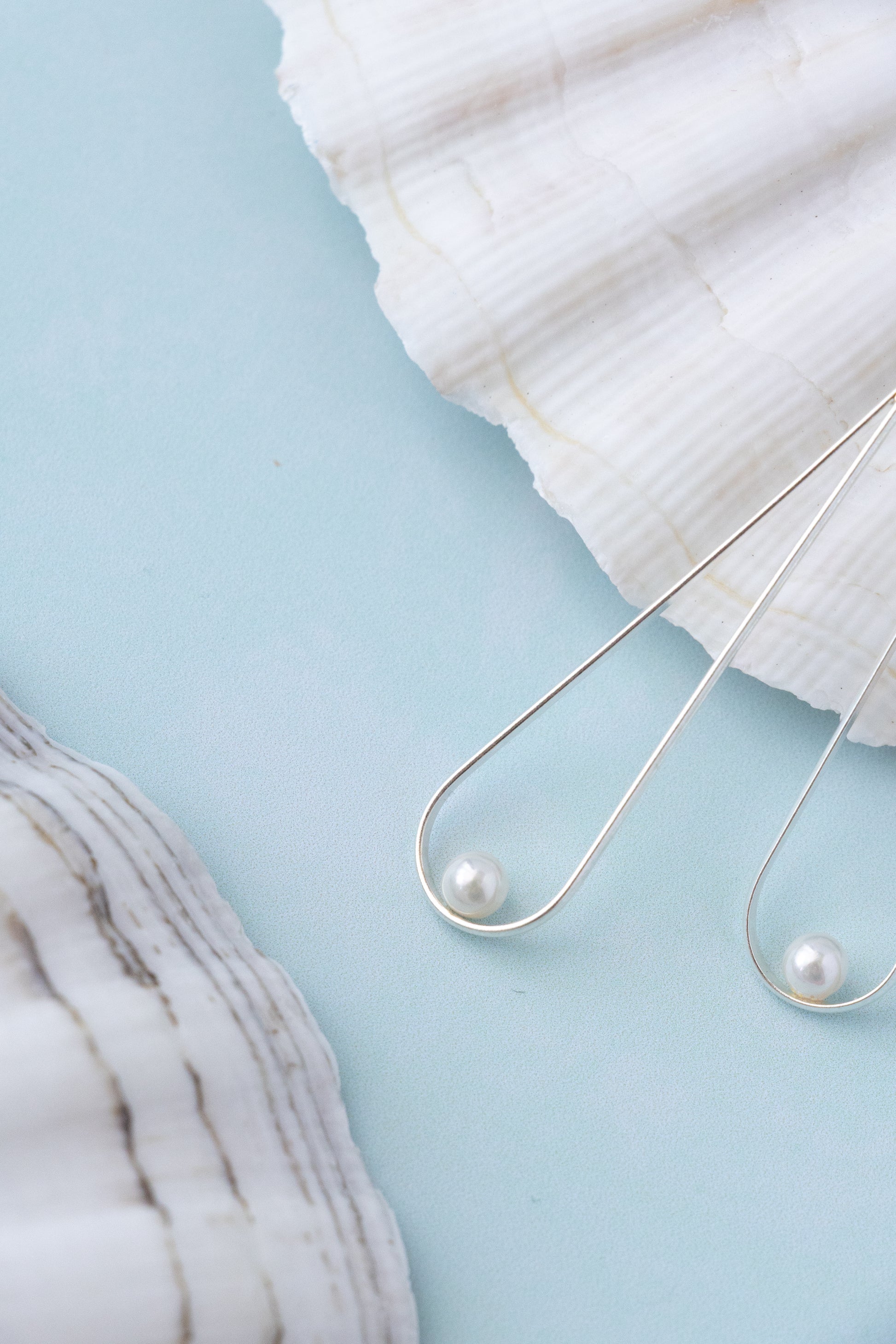 close uo to a silver drop shaped earring with a delicate pearl on blue background