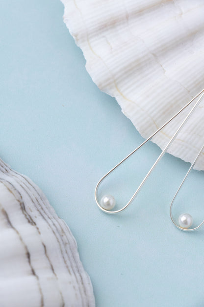 close uo to a silver drop shaped earring with a delicate pearl on blue background