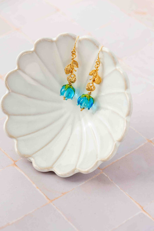 Gold earrings with blue flowers on a white shell-shaped dish.