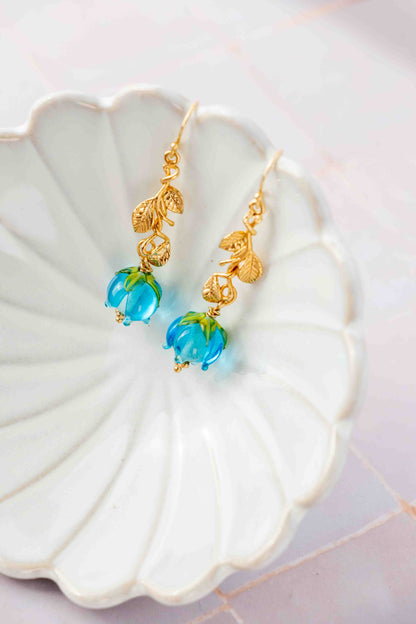 Gold earrings with blue roses on a white shell
