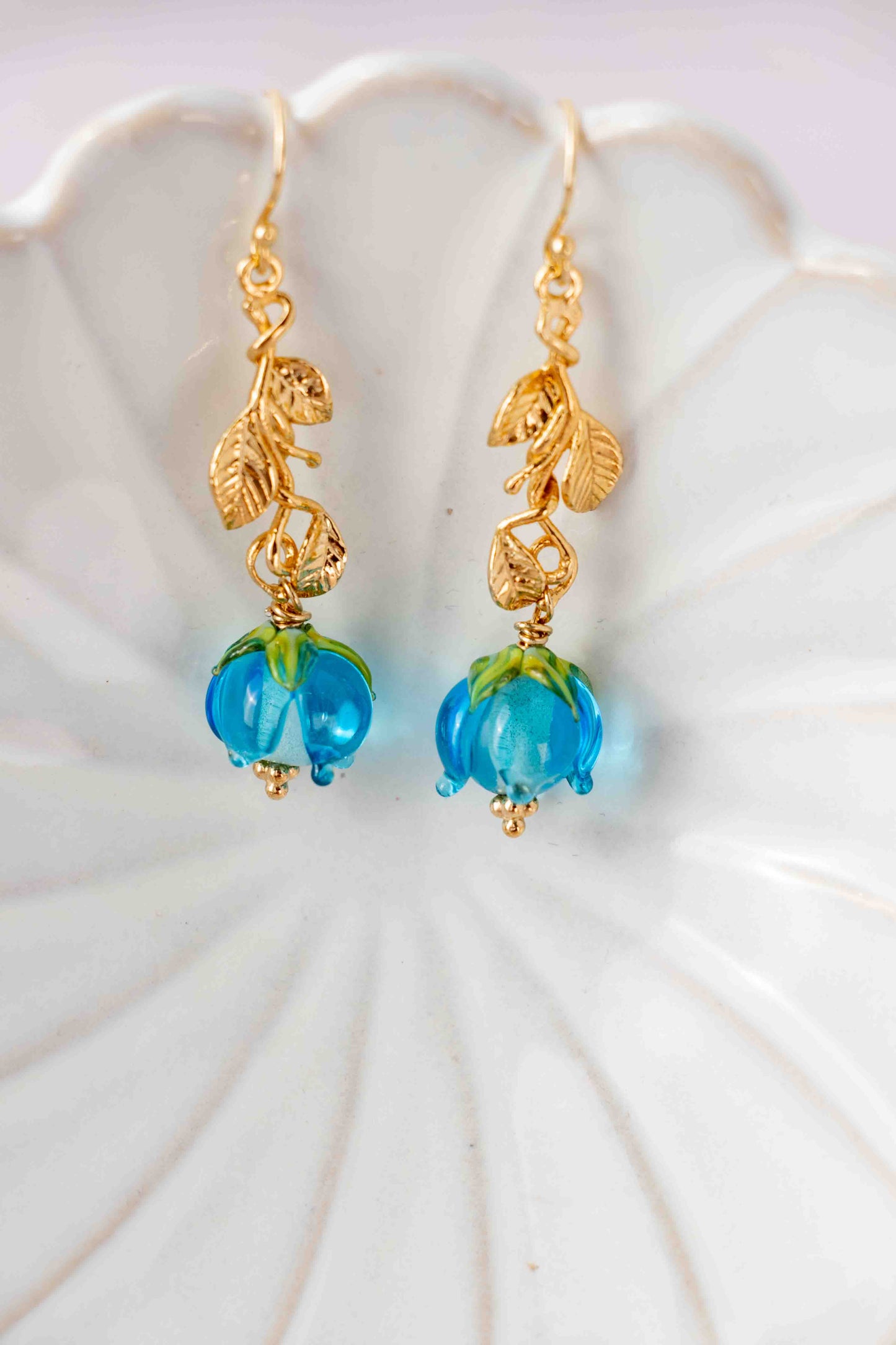 Gold earrings with blue roses on a white shell background