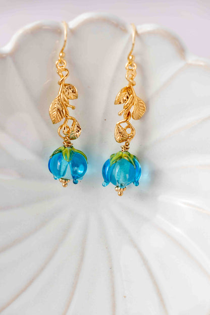 Gold earrings with blue roses on a white shell background