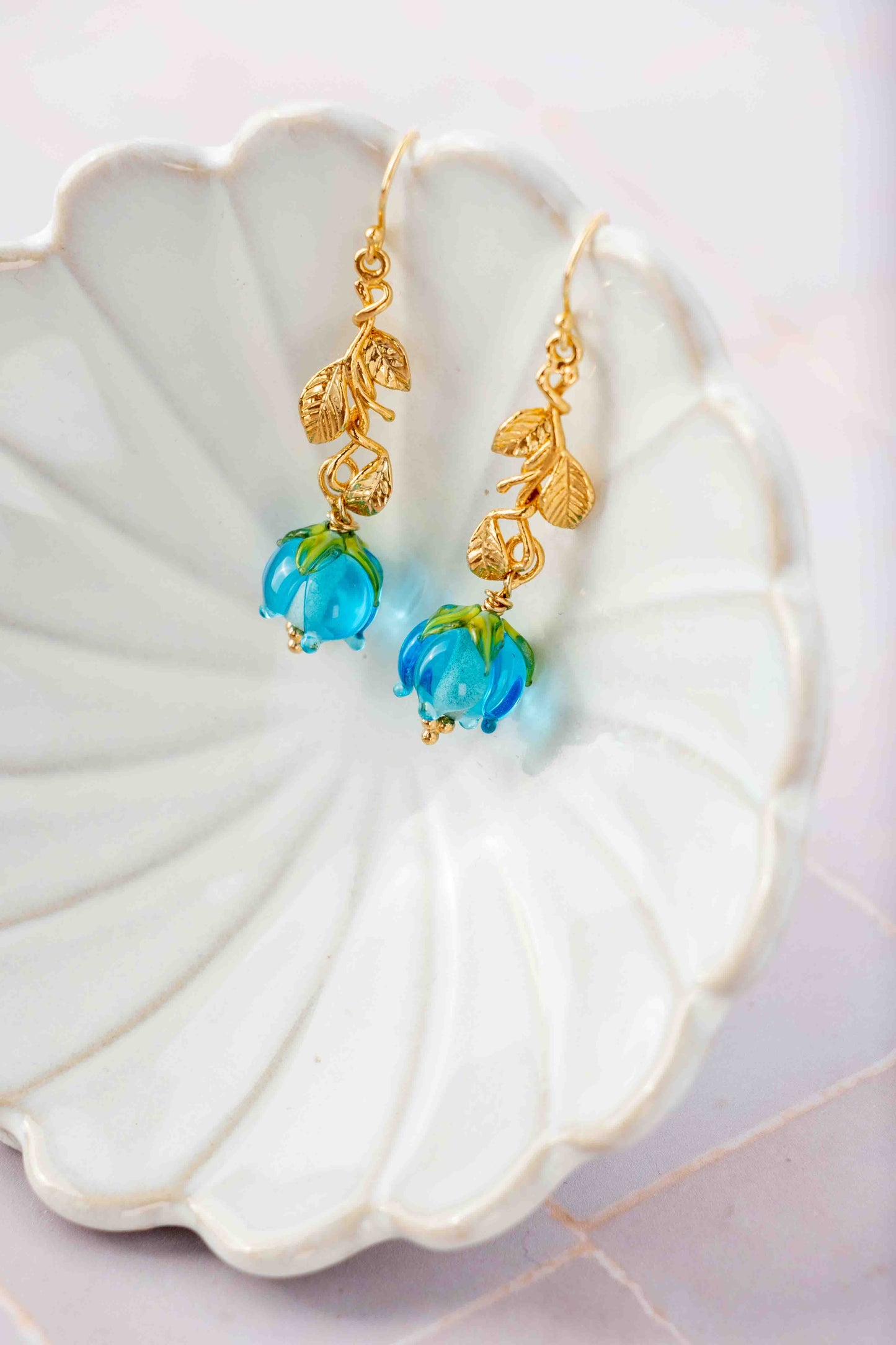 Gold earrings with blue rose flowers on a white shell