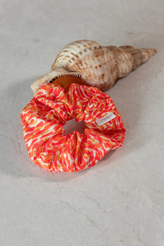 Orange and red patterned scrunchie with a shell on a light gray surface