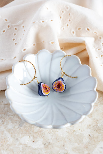 Pair of earrings with purple and orange figs on a white shell dish.