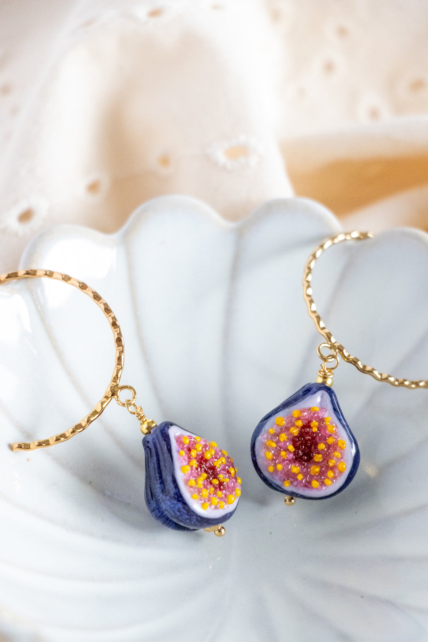Pair of earrings resembling blue figs with pink and yellow seeds on a white shell background