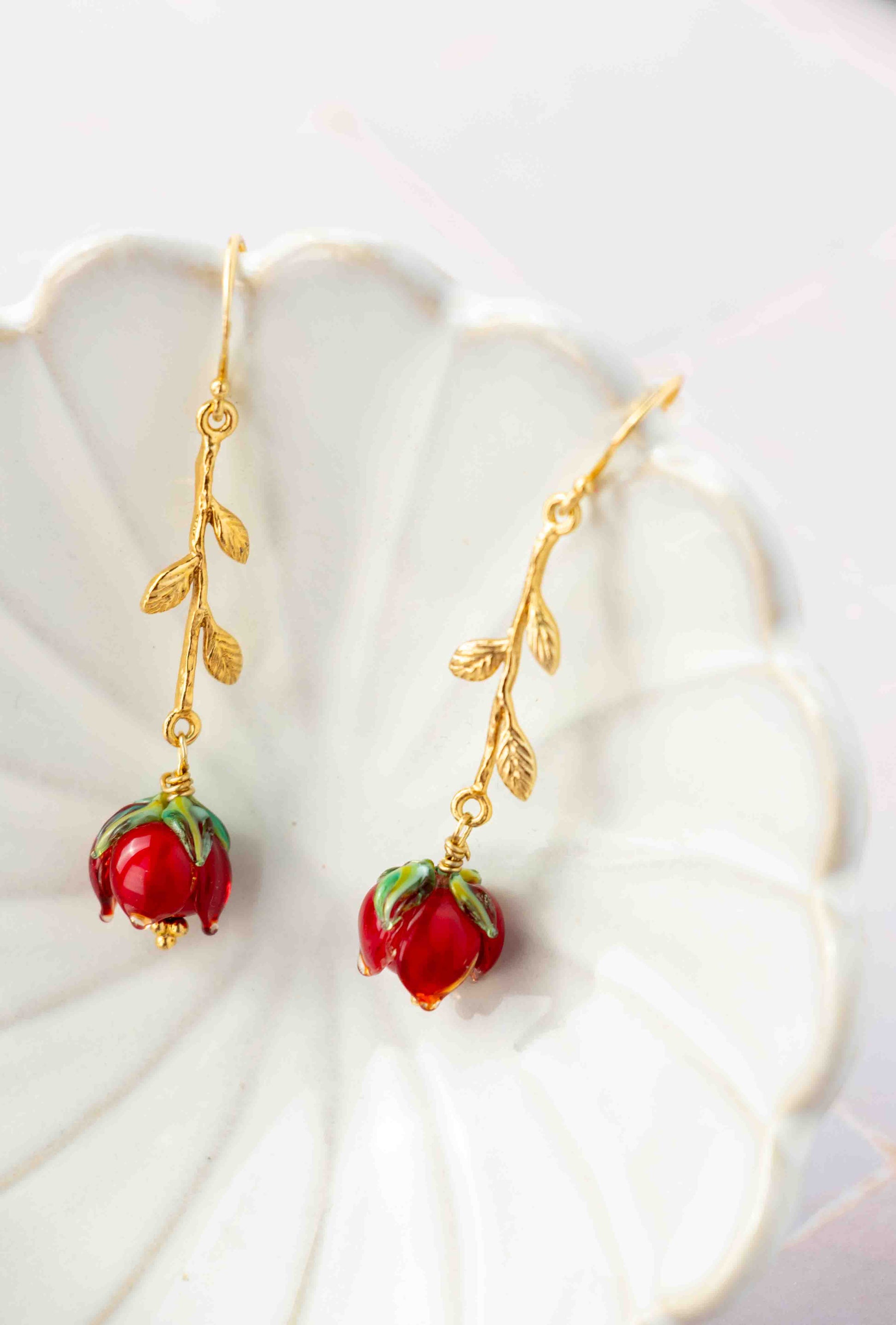 Gold earrings with red rose charms on a white shell background