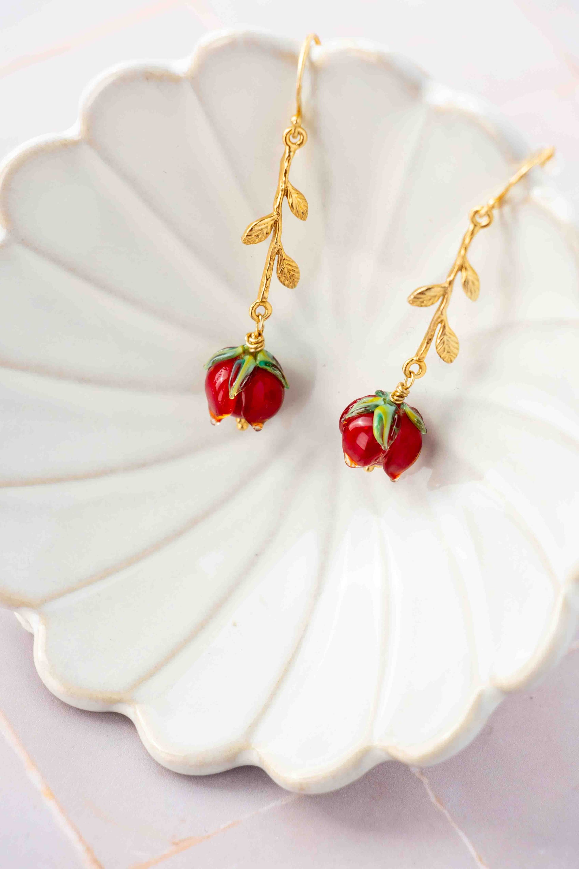 Gold earrings with red rose charms on a decorative white plate.