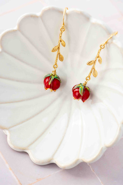 Gold earrings with red rose charms on a decorative white plate.