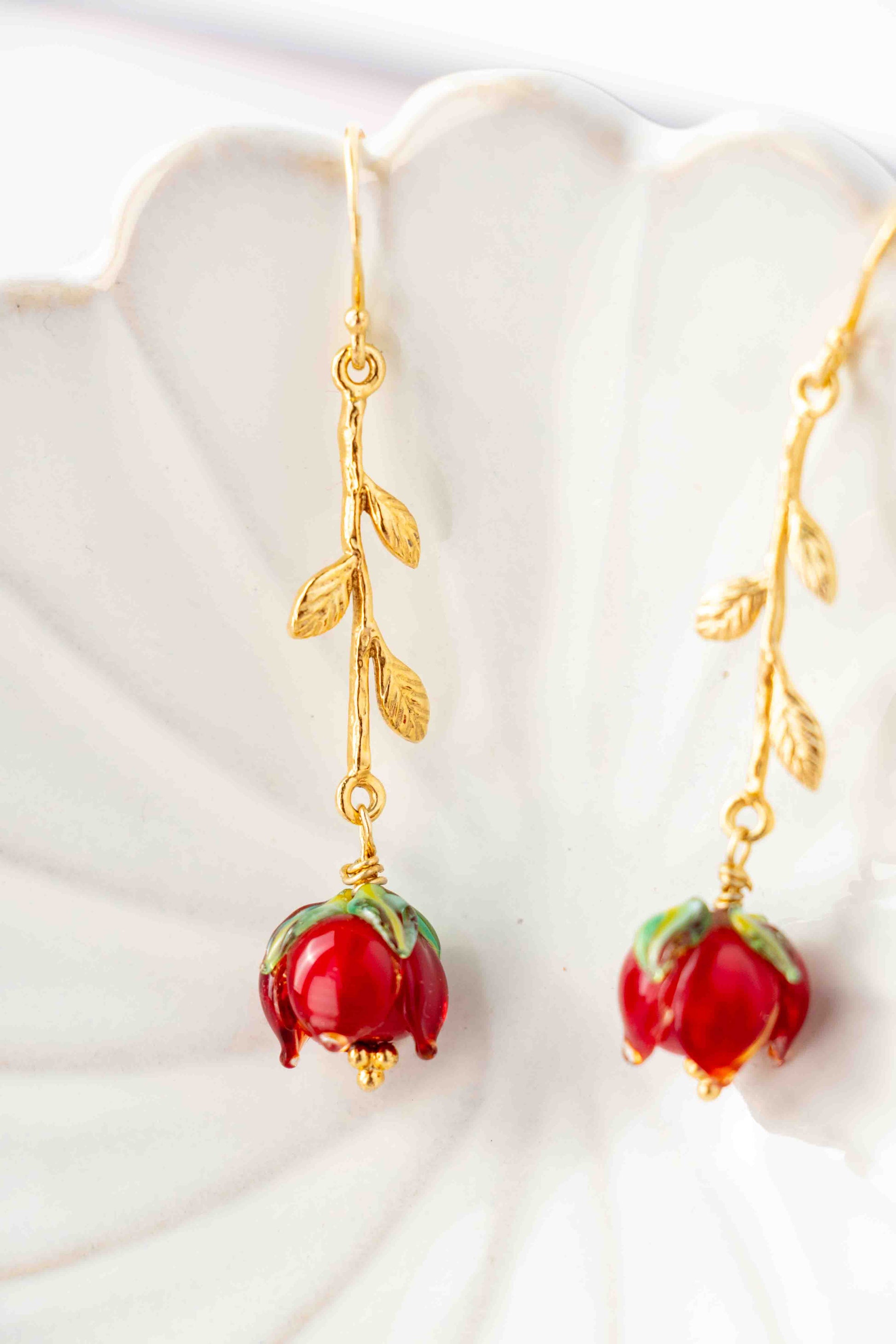 Gold earrings with red rose like charms on a white shell background