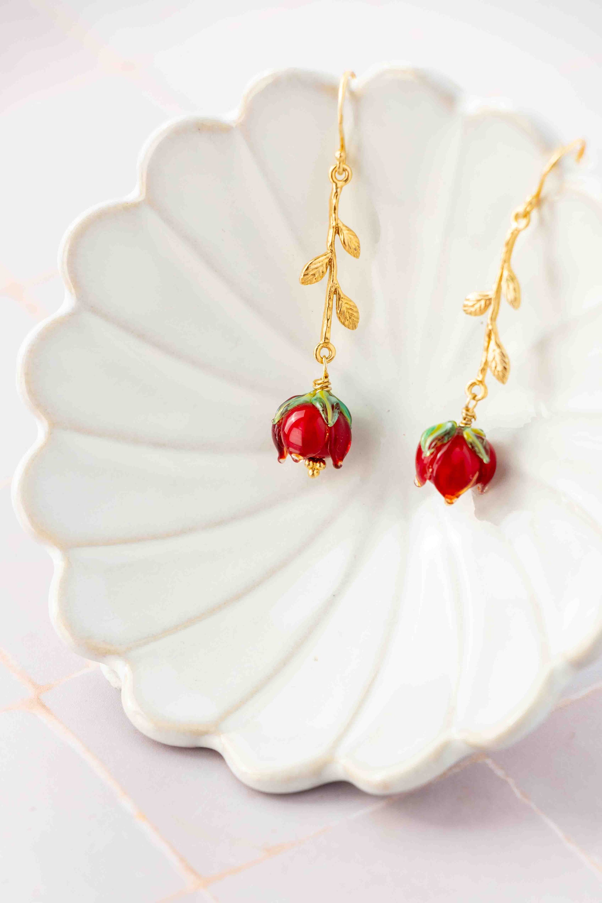Gold earrings with red roses charms on a white shell-shaped dish.