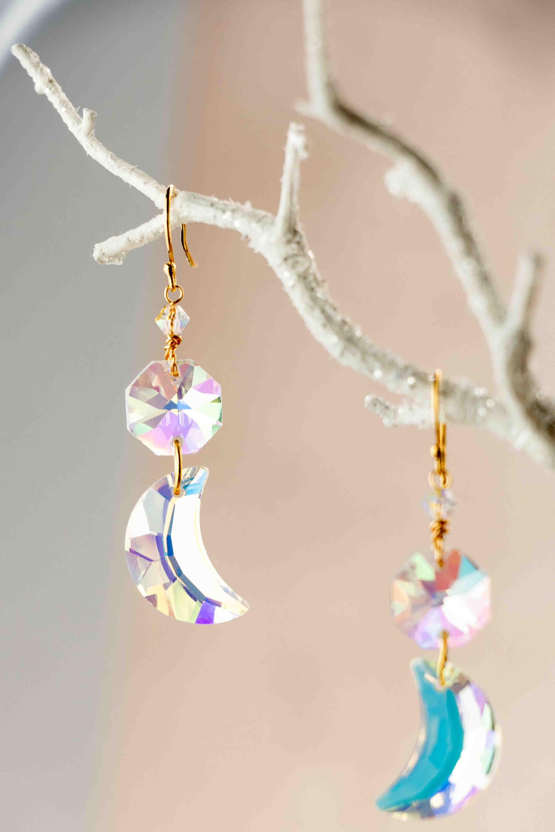 Crystal moon-shaped earrings hanging from a branch with a neutral background