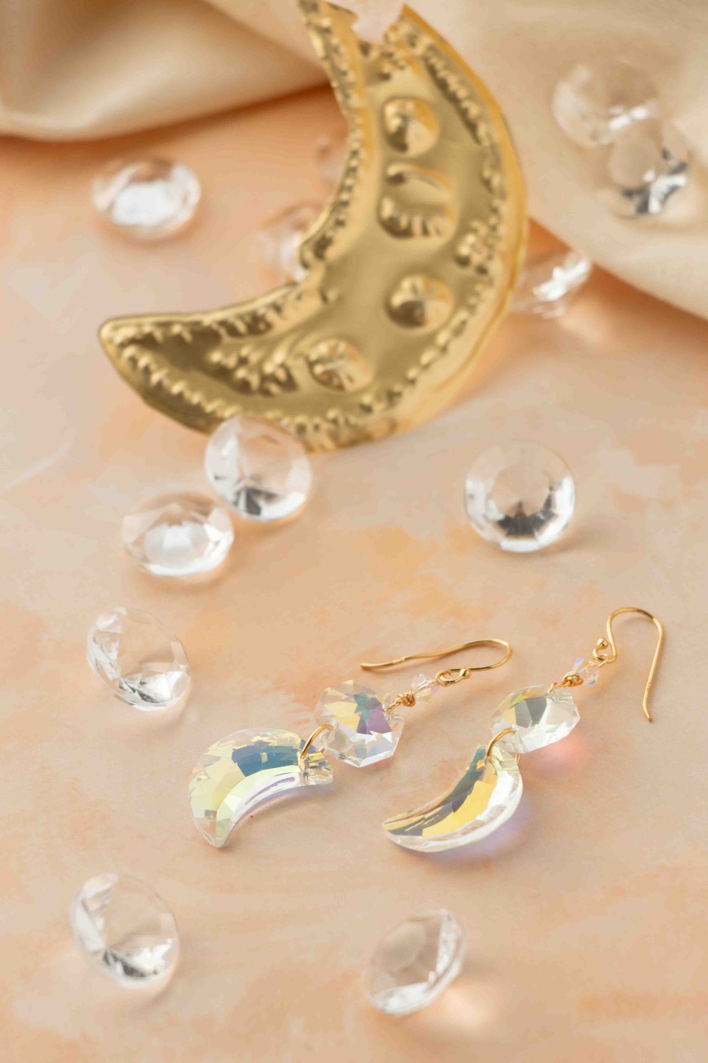 Gold moon-shaped earrings on a soft beige background with clear crystals.