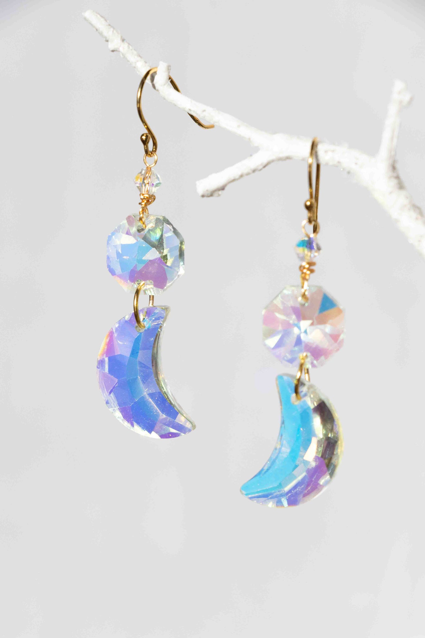 Iridescent moon-shaped earrings on a white branch background