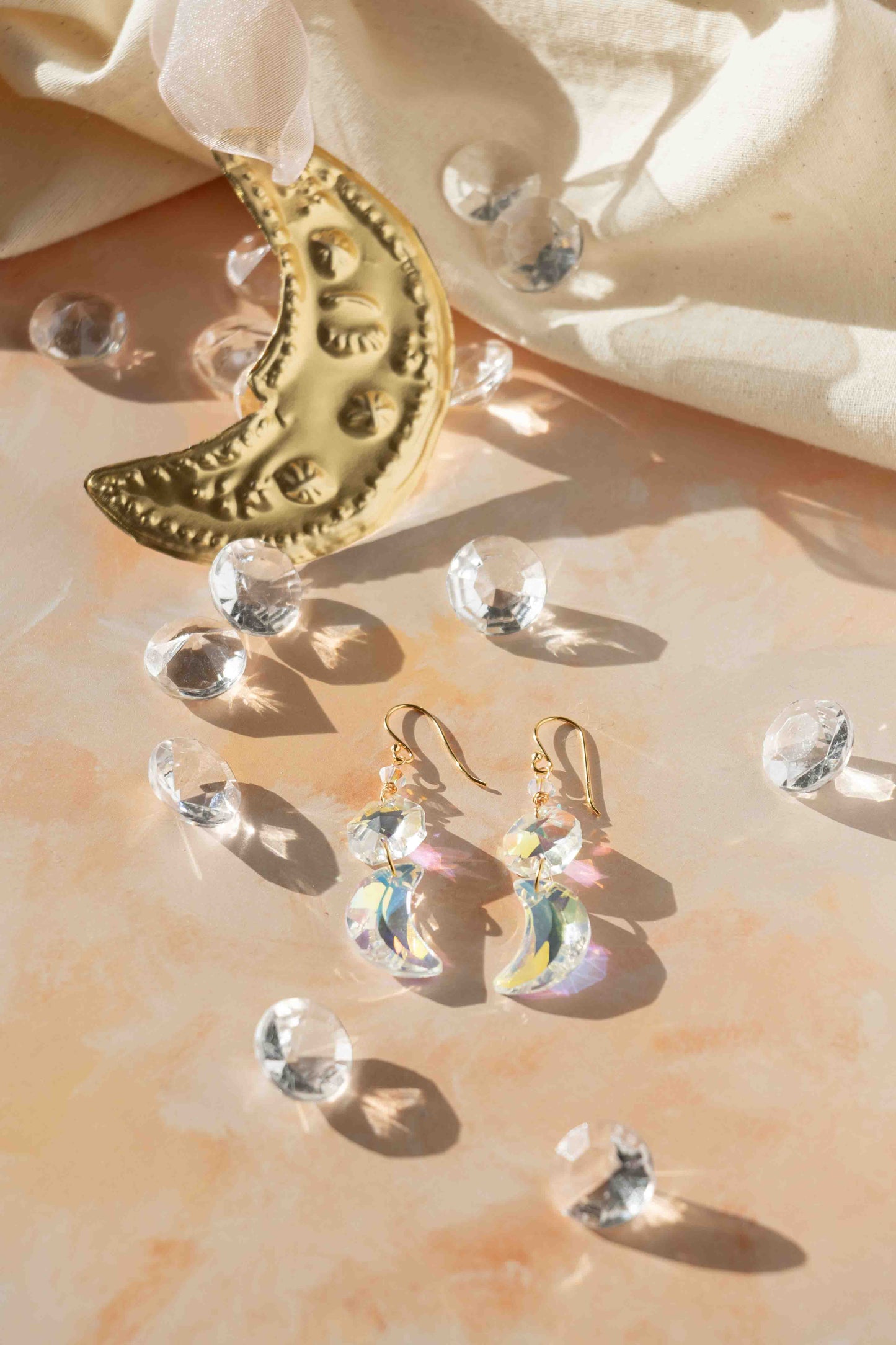 Gold crescent moon earrings with clear gemstones on a soft fabric background