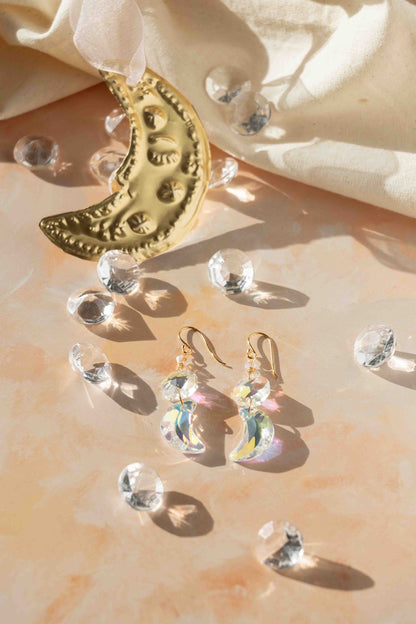 Gold crescent moon earrings with clear gemstones on a soft fabric background