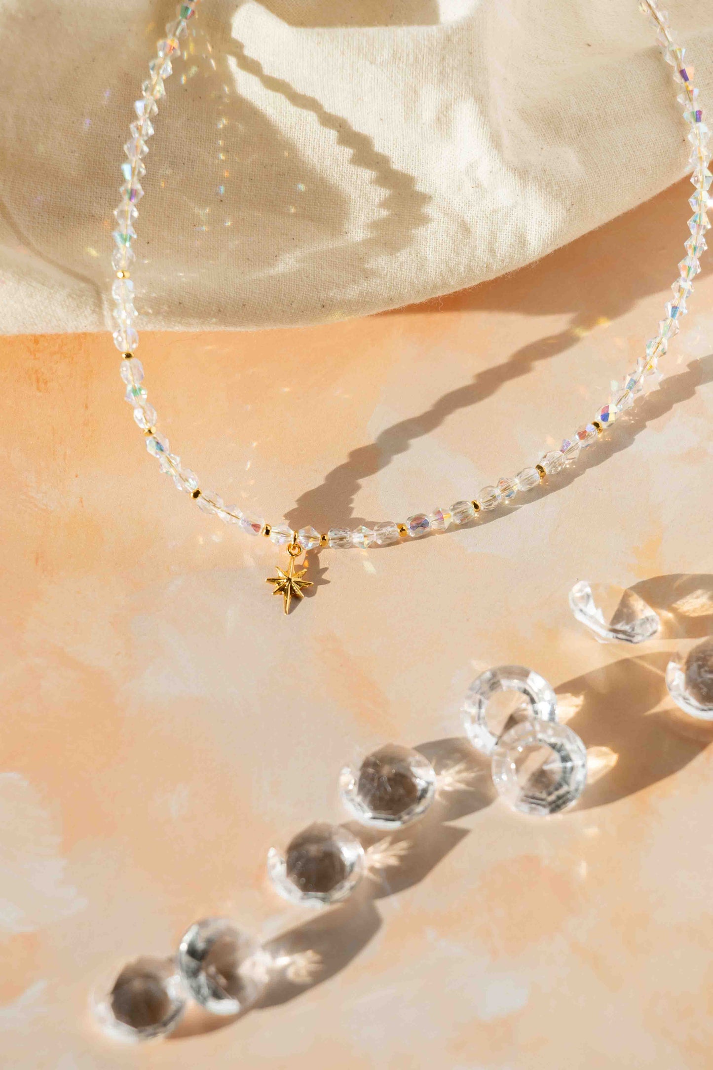 Necklace with clear beads and a gold charm on a beige surface