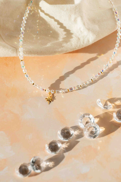 Necklace with clear beads and a gold charm on a beige surface