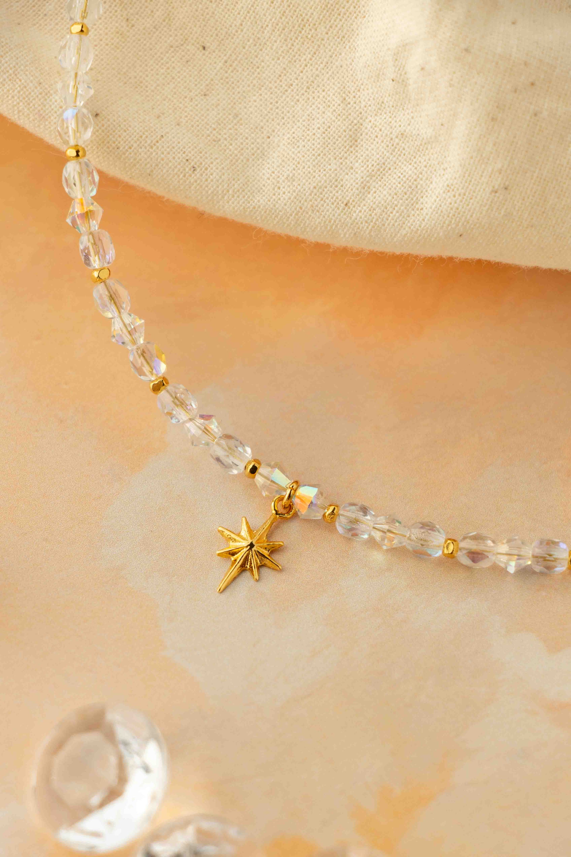 Necklace with clear beads and gold star charm on a beige background
