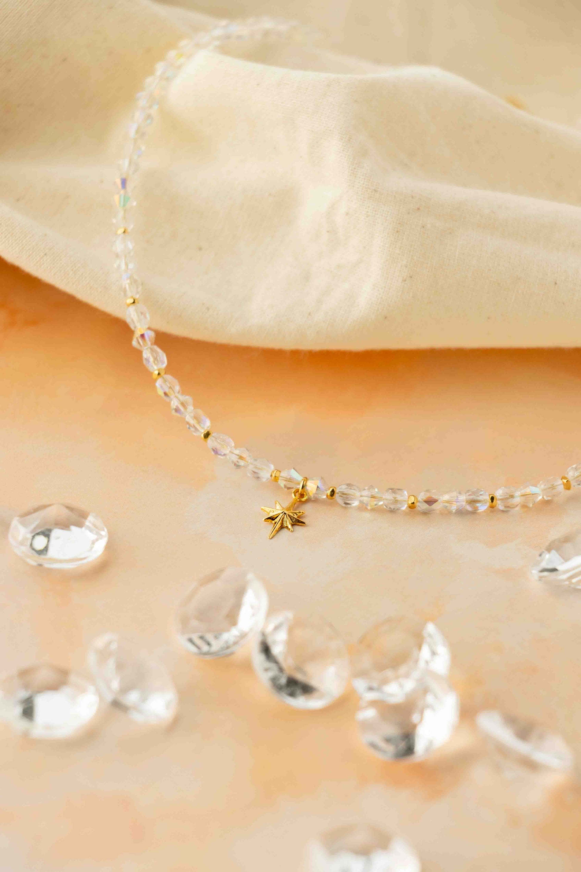 Delicate beaded necklace with a small gold star pendant on a beige fabric background.