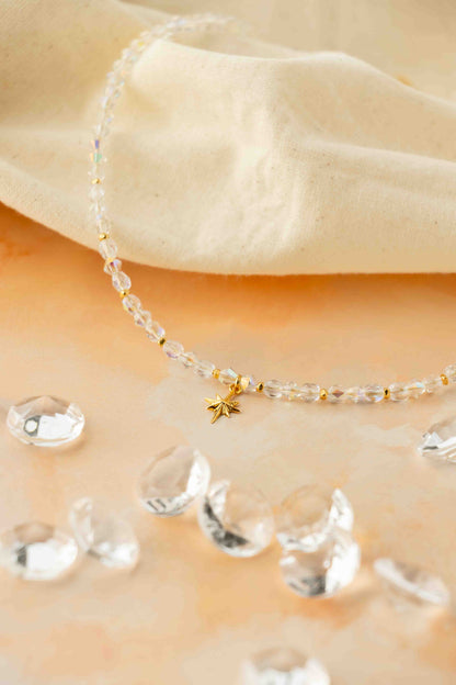 Delicate beaded necklace with a small gold star pendant on a beige fabric background.